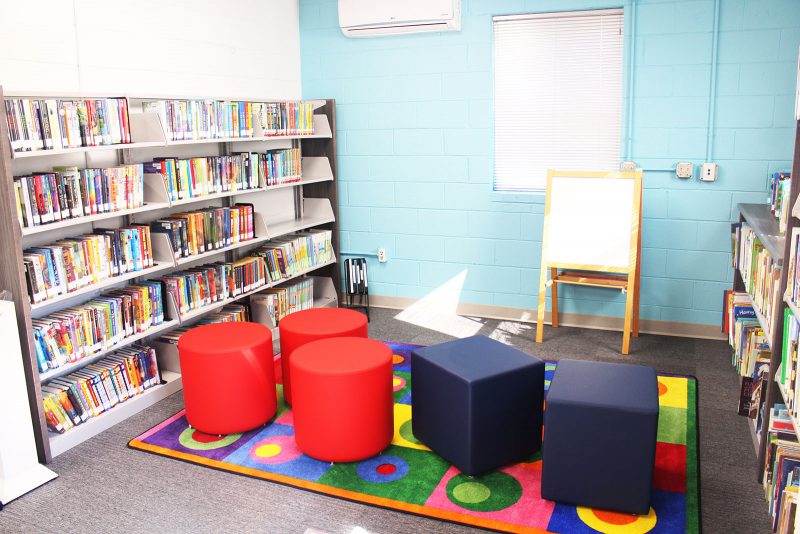 Children's area at Bragtown featuring comfortable seating, a colorful rug, a shelf of children's books, and 