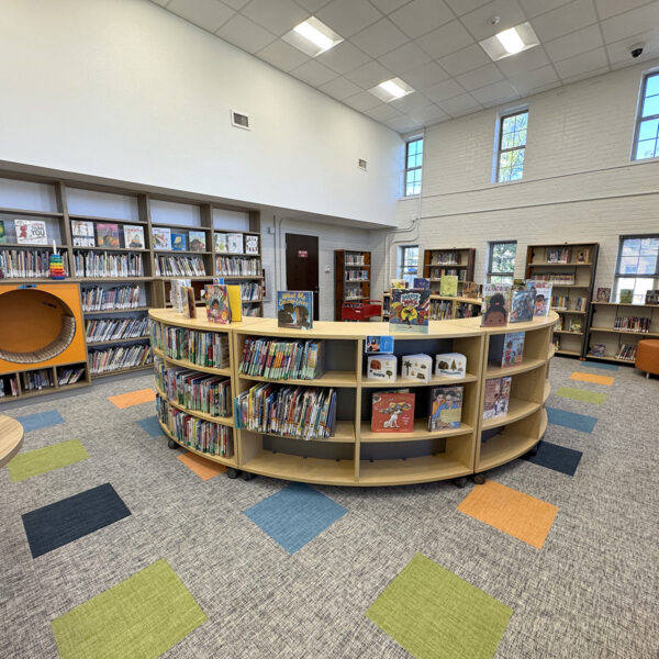 The children's area, a colorful space with a curved bookcase in the middle of the room, more bookshelves lining the walls, and a child-sized circular seat tucked among the shelves.