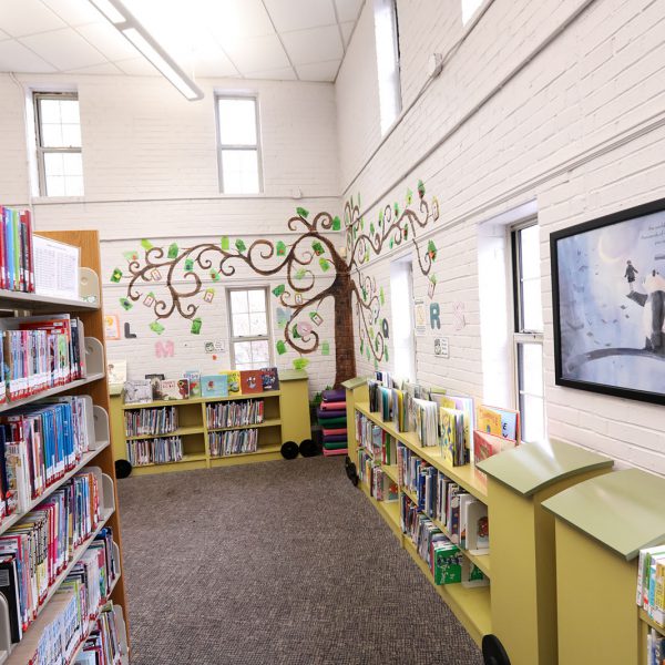Tree mural in the corner of the children's area, in the background past bookshelves and posters