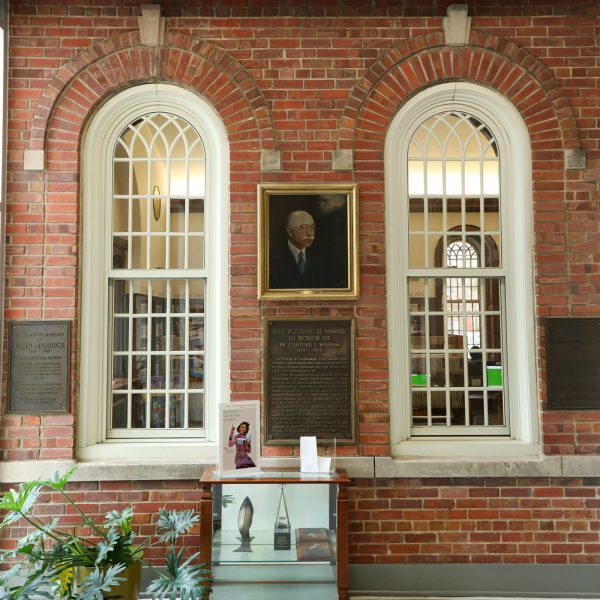 Painted portrait of Dr. Stanford L. Warren hanging above a plaque explaining that the building was named in his honor, set on a brick wall between two decorative interior windows