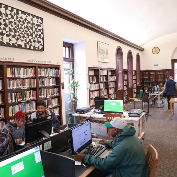 The main reading room at Stanford L. Warren, with people using public computers, tables and chairs, and bookshelves lining the walls