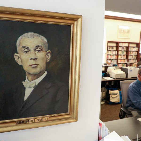 Painted portrait of Aaron McDuffie Moore, M.D., with the checkout desk and library staff visible in the background