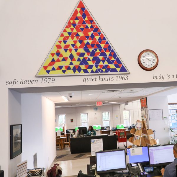 All the Possibilities of Three Into Four, by Vernon Pratt - a large, triangular, red yellow and blue painting with many geometric shapes. It hangs on the wall above an opening with the main checkout desk below and the children's area across the lobby