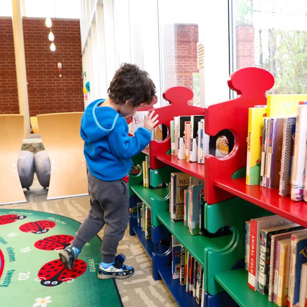 Young child browsing board books on a low, colorful shelf