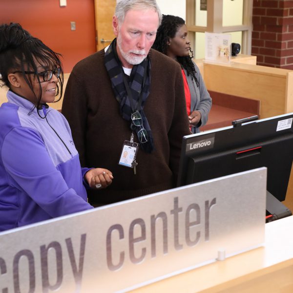 Librarian helping a woman with a computer behind a sign that says Copy Center