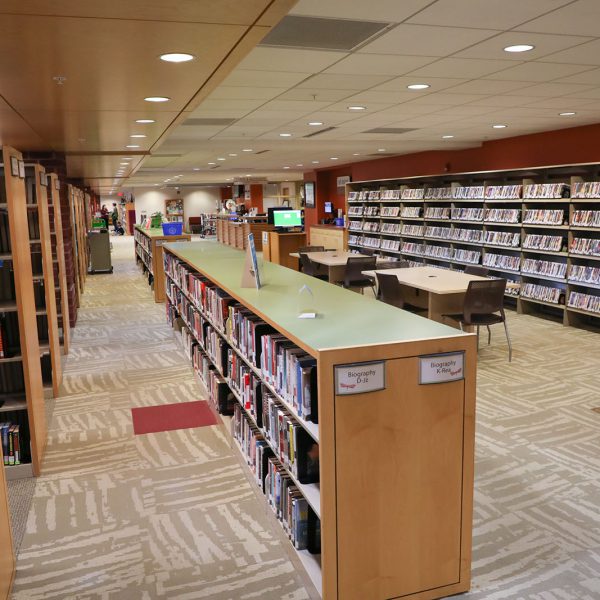 The open front area at East Regional, with shelves of books and DVDs, large tables with chairs, and the checkout desk in the backgroud