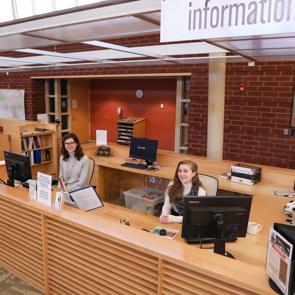 Librarians sitting at computers at a large desk under a sign that says "Information"