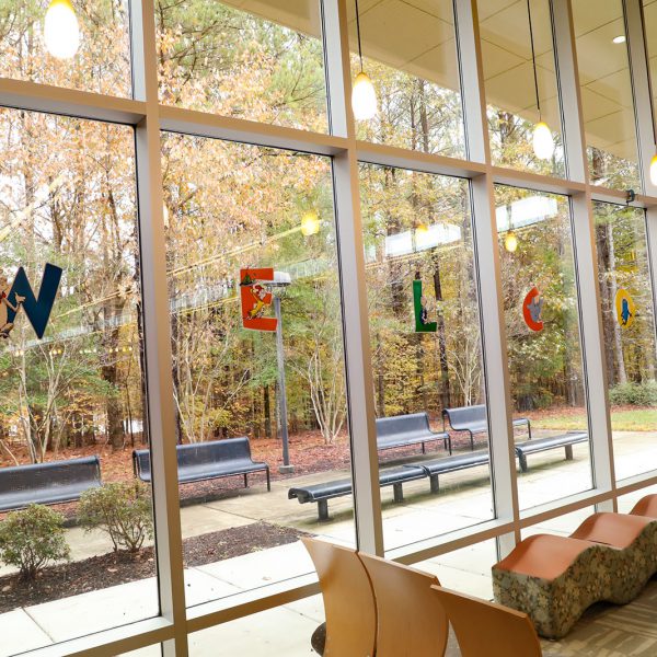 Wall full of tall windows. Each pane has a letter with a Dr. Seuss character, spelling out the word "Welcome." Seating is available indoors and out.