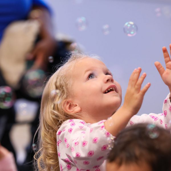 Young child reaching up to catch bubbles