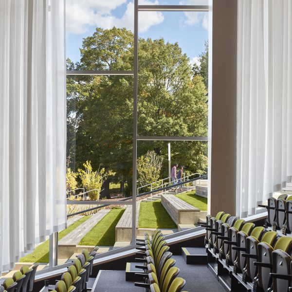 Rows of folded auditorium chairs. Outside the window, grassy amphitheater seating follows the slope of the indoor auditorium