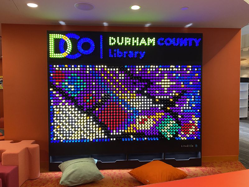 Six-foot-tall light wall, with the Durham County Library logo and an abstract design created in light pegs