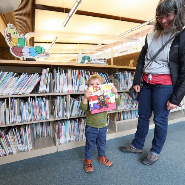 Parent with a small child holding up a book in front of a shelf full of children's books