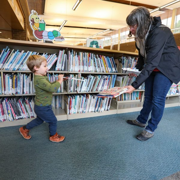 Child hurrying to add a book to a stack in his mother's hands