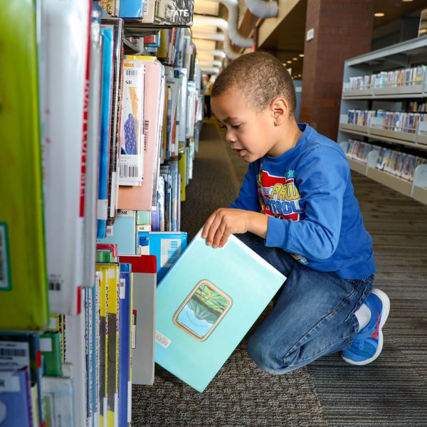A child kneels to select a book from a shelf