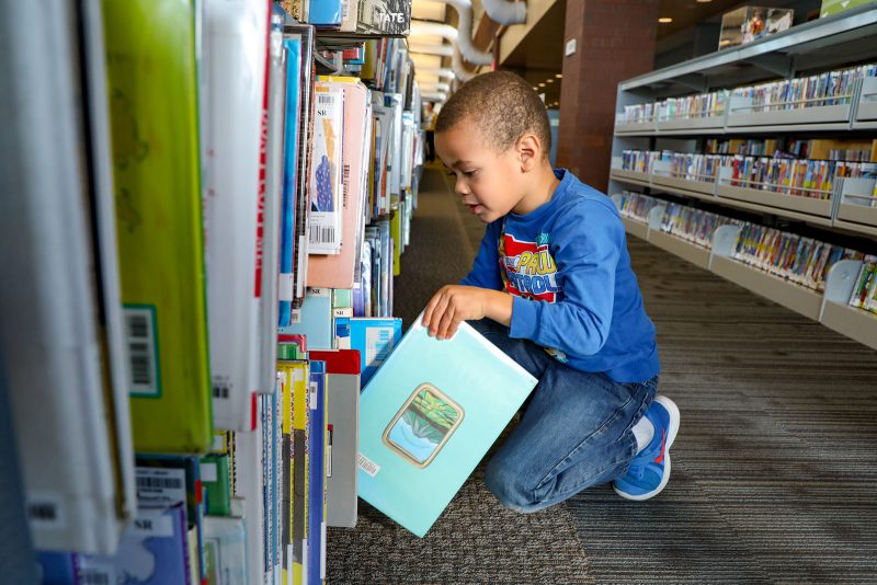 A child kneels to select a book from a shelf