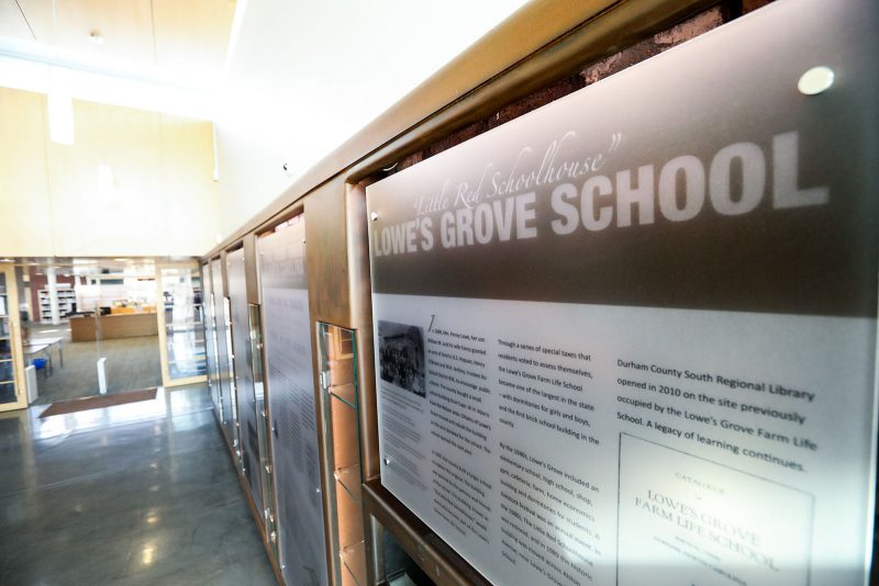 Display titled "Little Red Schoolhouse: Lowe's Grove School," with longer text underneath. Other similar signs line the rest of the wall