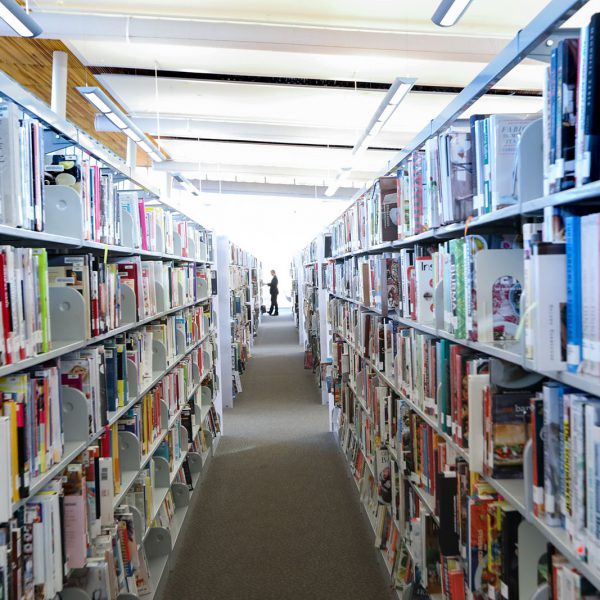 Long shelves of books, with a person standing at the end of the aisle
