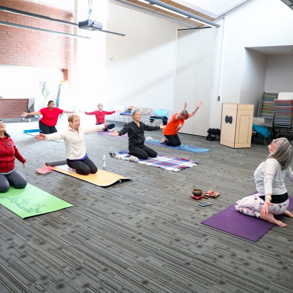 Yoga class with a group of people kneeling on mats and stretching in a large room