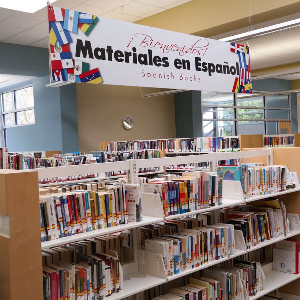 Bookshelves with sign saying "¡Bienvenidos! Materiales en Españoll / Spanish Books" overhead