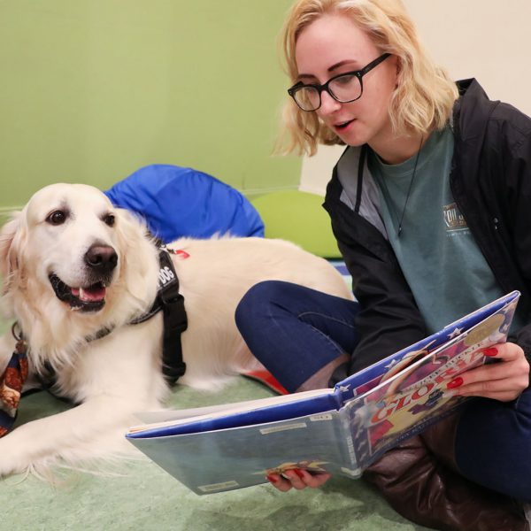 A teen reads a book to a visiting therapy dog