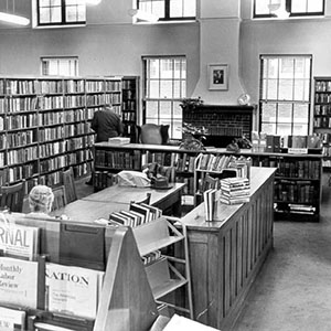 Black-and-white library interior, with bookshelves, windows, and staff working