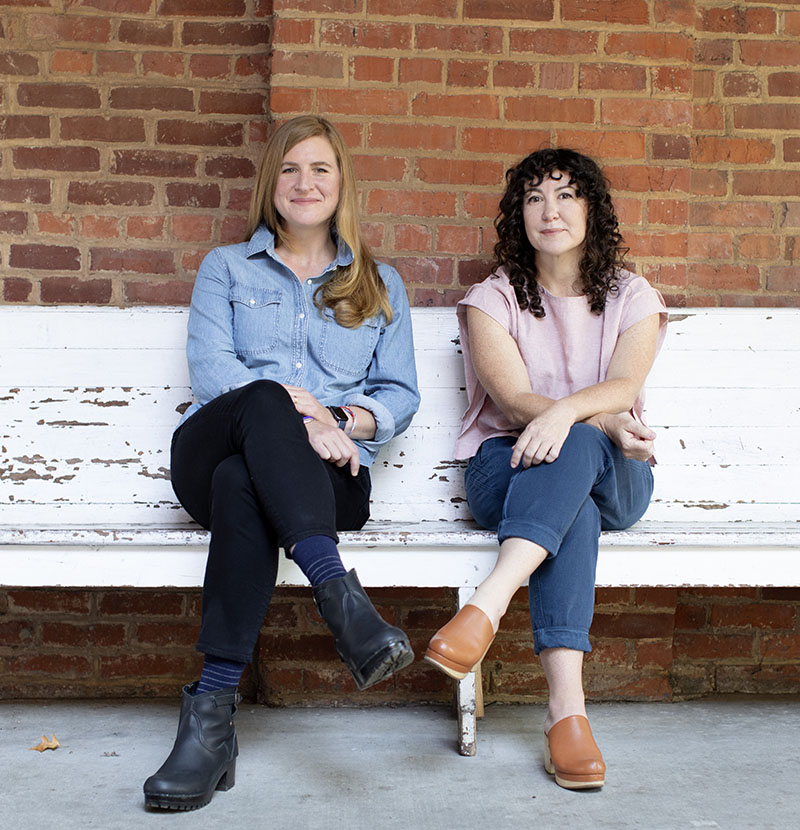 Lauren Spohrer and Phoebe Judge, hosts of Criminal podcast and presenters of this event, sit on a bench in front of a brick wall