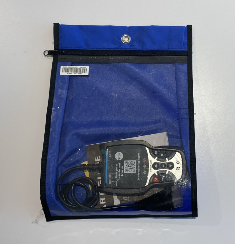 Blue zippered bag with a clear front, showing a diagnostic code reader inside. It's a black gadget with buttons on the top and a screen covered with a protective sheet including a QR code.