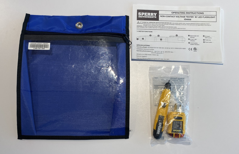 Yellow-and-black GFCI outlet tester and non-contact voltage tester with operating instructions. The empty blue zippered bag sits next to the kit.