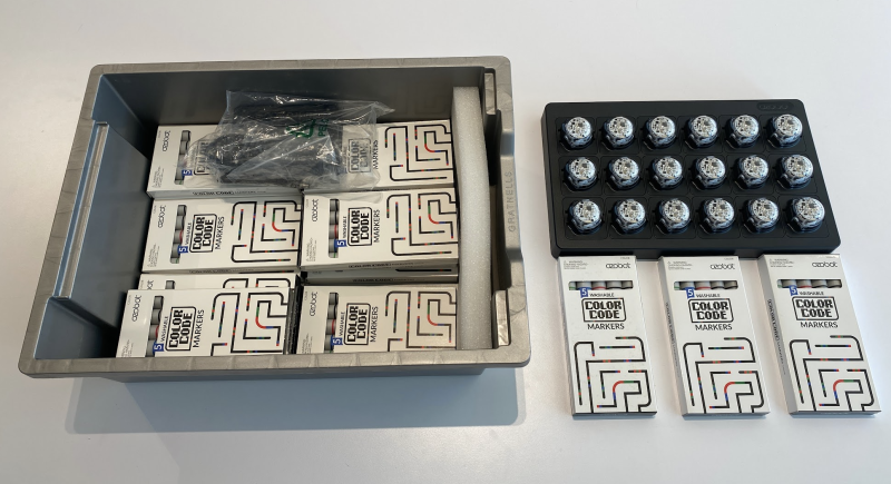 Opened bin showing a set of 18 small round robots, plus boxes of markers and a charger.