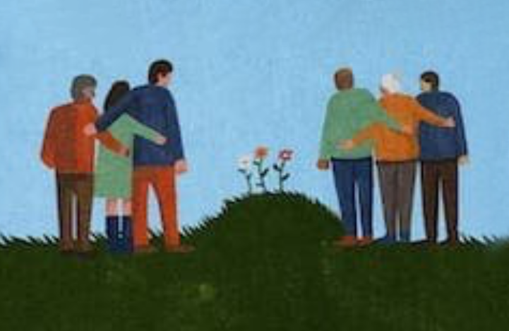 Group of people standing with arms around each other in consolation, looking at a mound of grass with flowers growing on top.