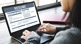 View over a woman's shoulder as she types on a laptop with a document titled résumé on the screen.