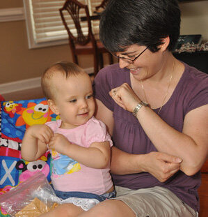 A smiling adult and baby sitting together and communicating via sign language.