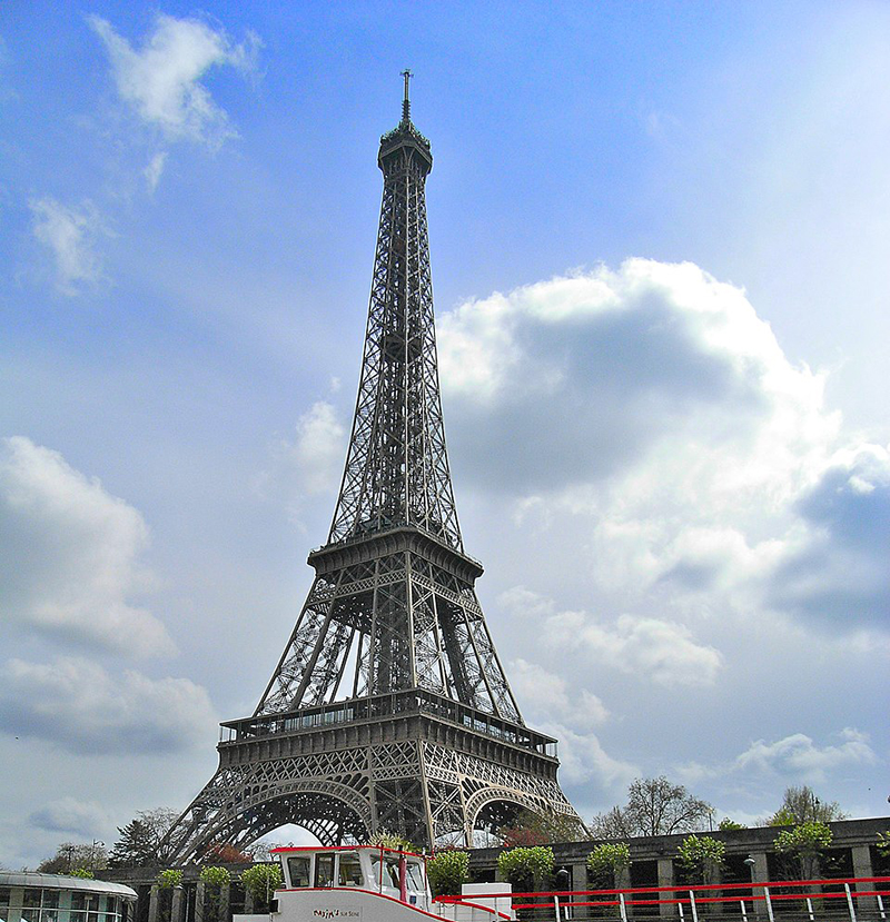 The Eiffel Tower against a blue sky with white clouds.