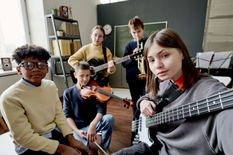 A multi-racial group of adolescents holding musical instruments including a trumpet, guitars, and a violin as if they're just about to start playing.