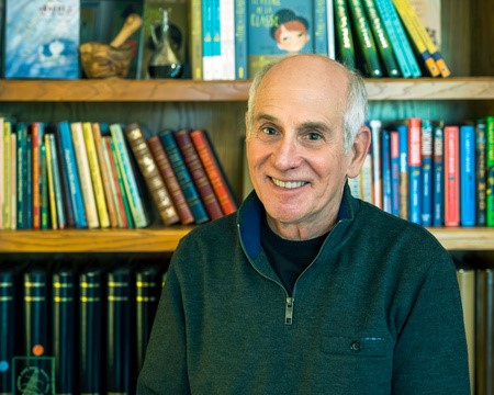 Author Louis Sachar smiles in front of loaded bookshelves.