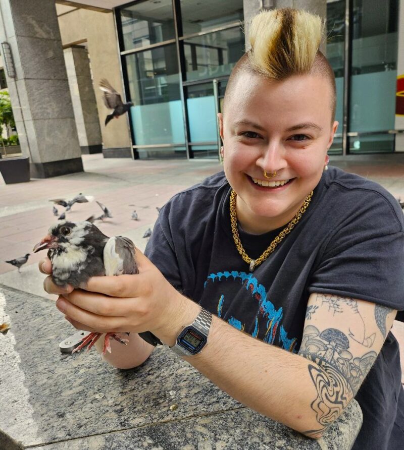 Faye holding a pigeon with two hands. Both are looking at the camera and smiling.