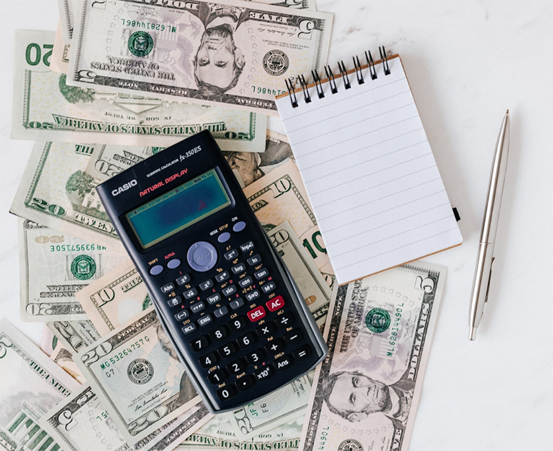 A calculator and notepad on top of a pile of cash.