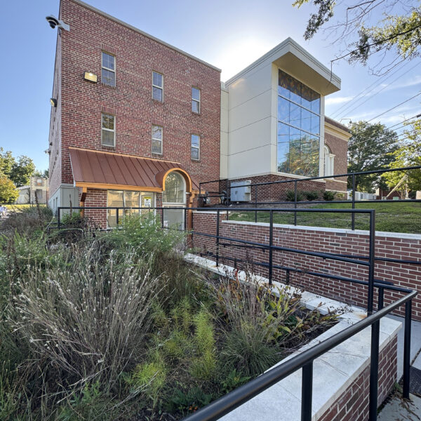Exterior of the back of the building. A full-height wall of windows extends from the center of the brick facade. A pollinator garden with native plants is in the foreground.