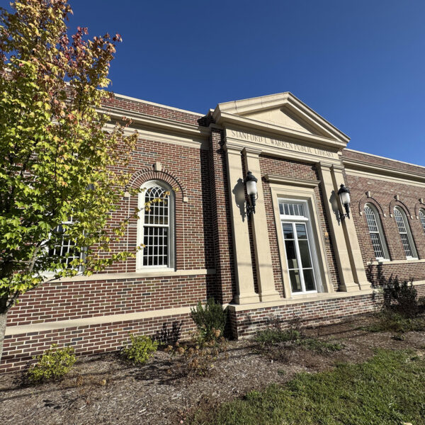The historic facade of Stanford L. Warren Public Library, with a classical-style concrete portico set into the brick wall and a row of arched windows.