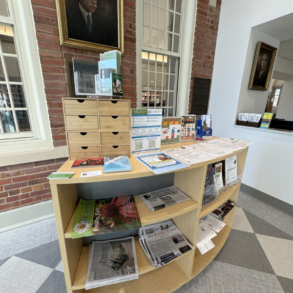 The lobby at Stanford L. Warren. A framed portrait of the building's namesake hangs on the wall. Wooden shelves hold flyers and free publications for distribution.