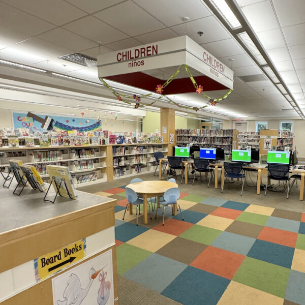 The children's area, a colorful space with checkered carpeting, child-sized seating, tables with computers, and varying heights of shelves full of books.