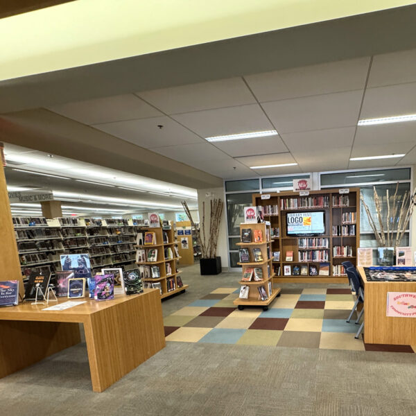 A central space with various books on display, a table holding a community jigsaw puzzle, and a screen displaying information about library events hanging on the wall.