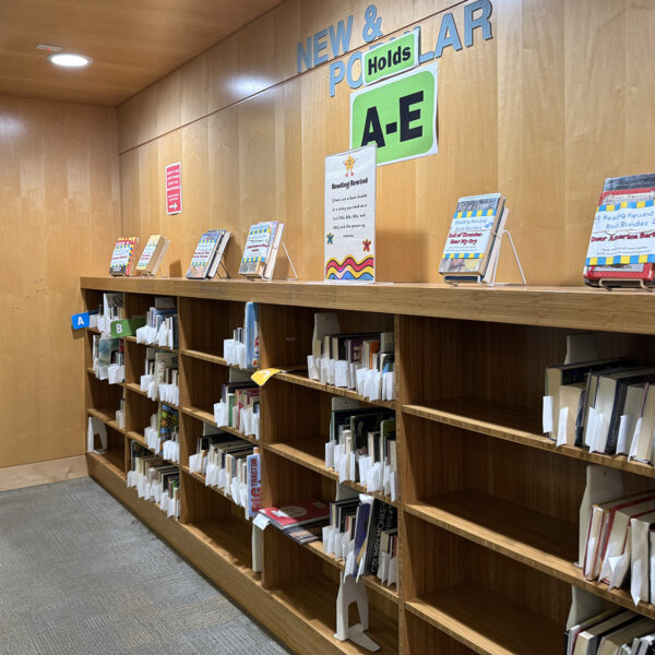 A low bookshelf next to the building entrance with items on hold for patrons.